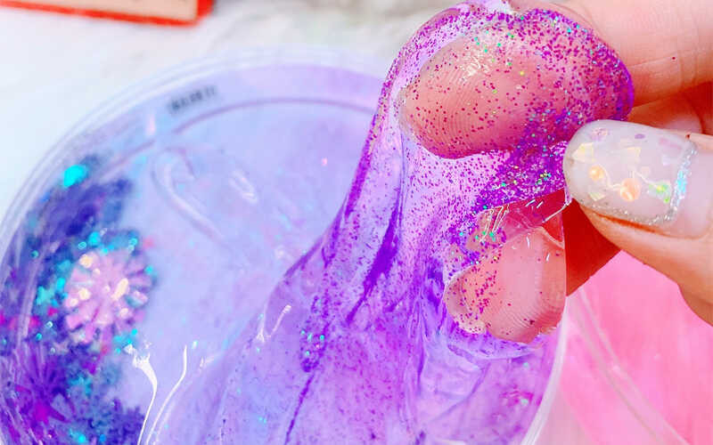 Một khối slime màu hồng dẻo mềm, được kéo giãn thể hiện đặc tính của đồ chơi slime tự làm.