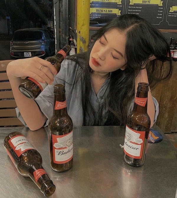 Quang cảnh thành phố về đêm qua khung cửa sổ, người ngồi nhậu một mình với ly rượu.