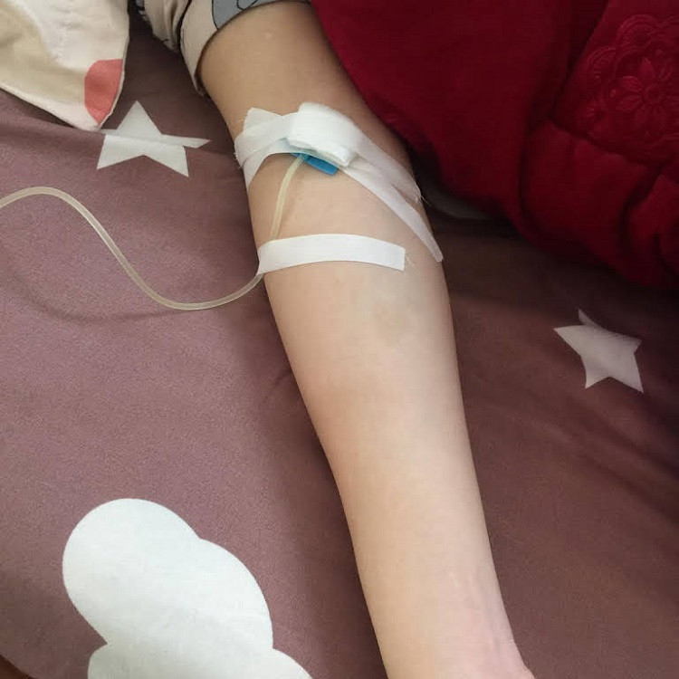 Tay một bệnh nhân đang truyền nước trong không gian phòng bệnh, thể hiện sự tĩnh dưỡng.