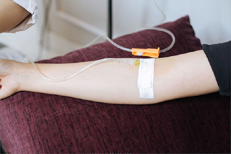 Bàn tay đang truyền nước với nền là ga trải giường bệnh viện màu trắng.