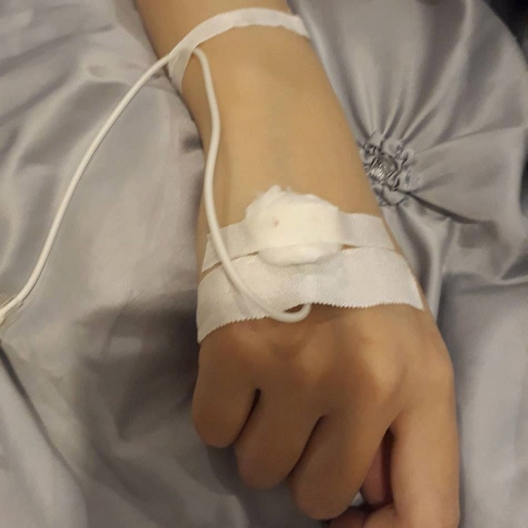 Một góc ảnh tay bệnh nhân nữ đang truyền nước, thể hiện sự tĩnh lặng trong phòng bệnh.